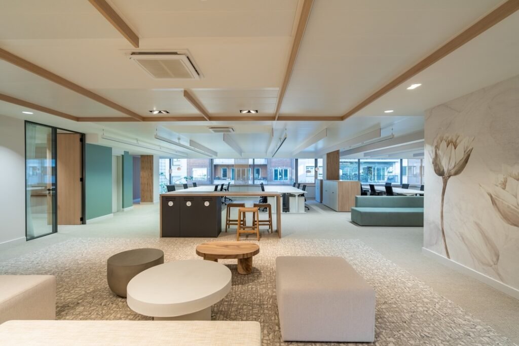 Espacio de oficina abierta con áreas de colaboración y lounges modernos, mobiliario modular en tonos neutros y detalles de diseño, ideal para trabajo flexible y reuniones informales.