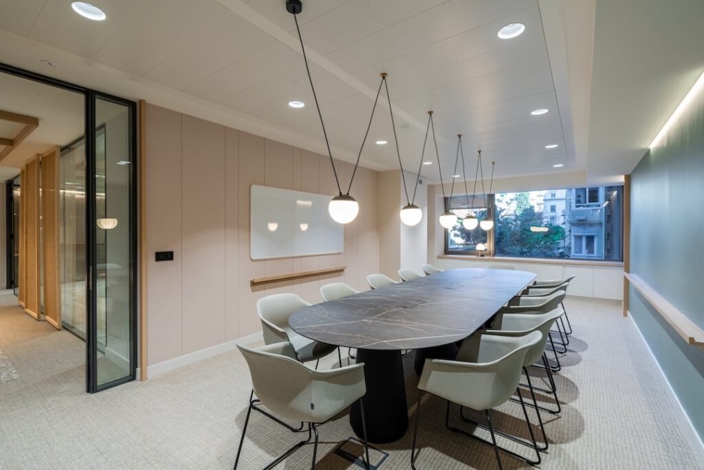Sala de reuniones privada y moderna en oficina flexible con mesa grande ovalada de mármol, sillas ergonómicas, iluminación colgante contemporánea y pizarra blanca, ideal para reuniones confidenciales.