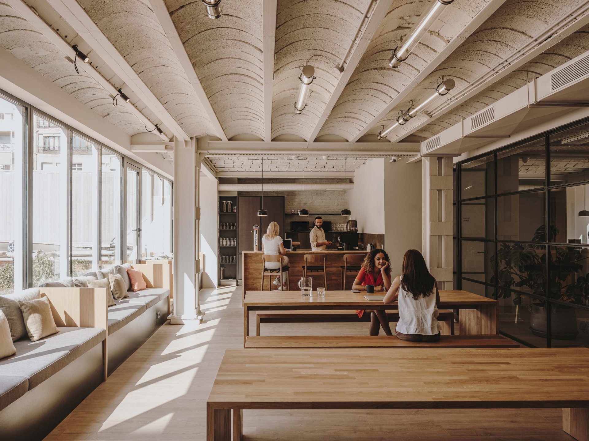 Zona común de unas oficinas para startups con luz natural y mesas de madera, donde un equipo colabora. Un buen diseño es clave en el checklist al buscar oficina.